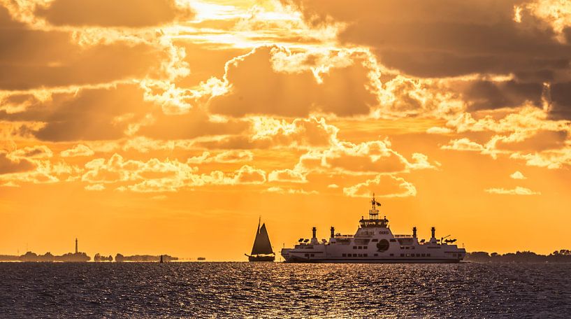 Zonsondergang met zeilboot en veerboot op het Wad van Martijn van Dellen