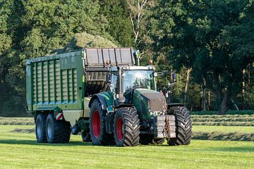 Groene tractor die gemaaid gras opraapt met een groene opraapwagen in de zomer in Nederland van Tonko Oosterink