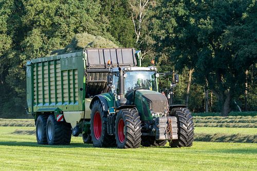 Groene tractor die gemaaid gras opraapt met een groene opraapwagen in de zomer in Nederland