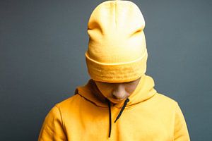 un adolescent élégant avec un sweat à capuche jaune baisse la tête