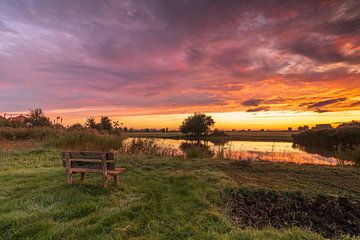 Genieten van de kleurrijke zonsopkomst op een houten bankje bij de Poelboerderij in Wormer van Bram Lubbers