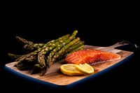 Fresh green asparagus, raw salmon and lemon slices on a wooden plank