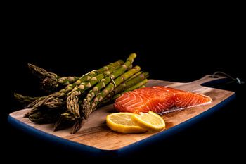 Verse groene asperges, rauwe zalm en schijfjes citroen op een houten plank
