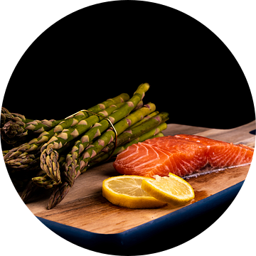 Verse groene asperges, rauwe zalm en schijfjes citroen op een houten plank van Dafne Vos