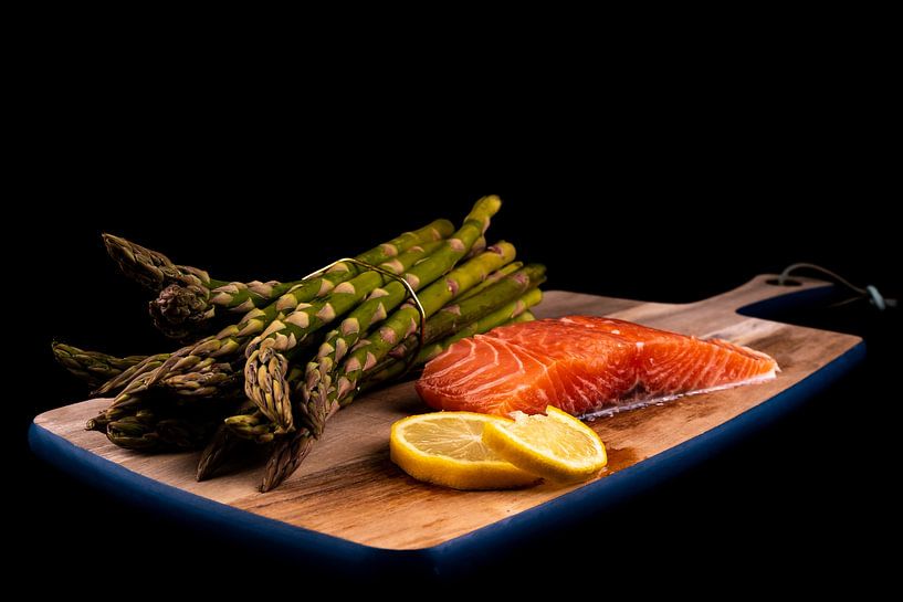 Fresh green asparagus, raw salmon and lemon slices on a wooden plank by Dafne Vos