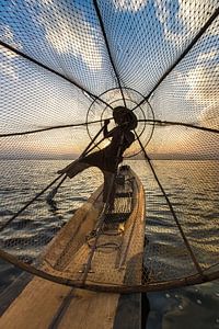 Visser die met traditionele boot op het Inle meer in Myanmar op ouderwetse wijze met een vis korf vi