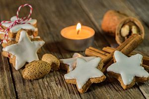 Kerstster koekjes, kaneelkruiden, noten en kaarslicht op houten tafel van Alex Winter
