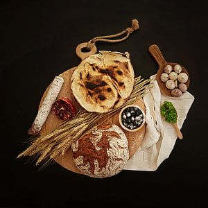 Stilleben mit Brot, Salami, Heidelbeeren und Knoblauch.