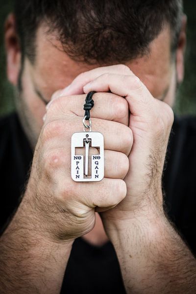 Homme priant avec le pendentif &quot;no pain no gain&quot; ; par Marcel Mooij