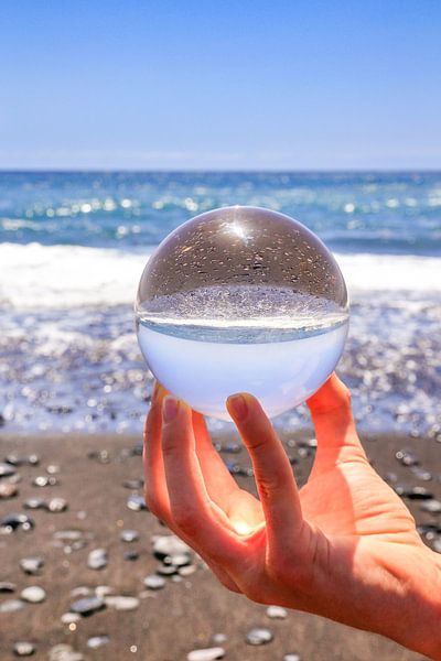 Hand holding crystal ball at beach and sea by Ben Schonewille