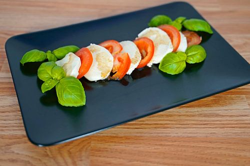 Tomaat, basilicum en mozarella met balsamico op een zwart dienblad