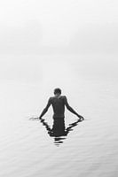 A boy stands in a lake shrouded in fog.