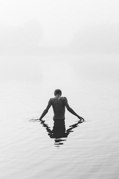 Een jongen staat in een meer dat gehuld is in mist. van Robin van Steen