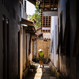 Oude dame wandelt door het dorp in traditionele Indonesische batik kleding. van Jeroen Cox