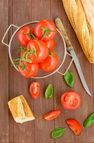 Frische Tomaten liegen in einem Küchensieb auf einem Holztablett