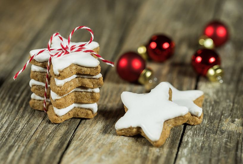 Stack of christmas star biscuits on wood background with red baubles by Alex Winter