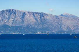 Blue seascape with sailboats and mountains in the background