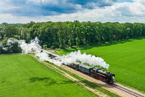 Stoomtrein met rook van de locomotief rijdt tussen de velden