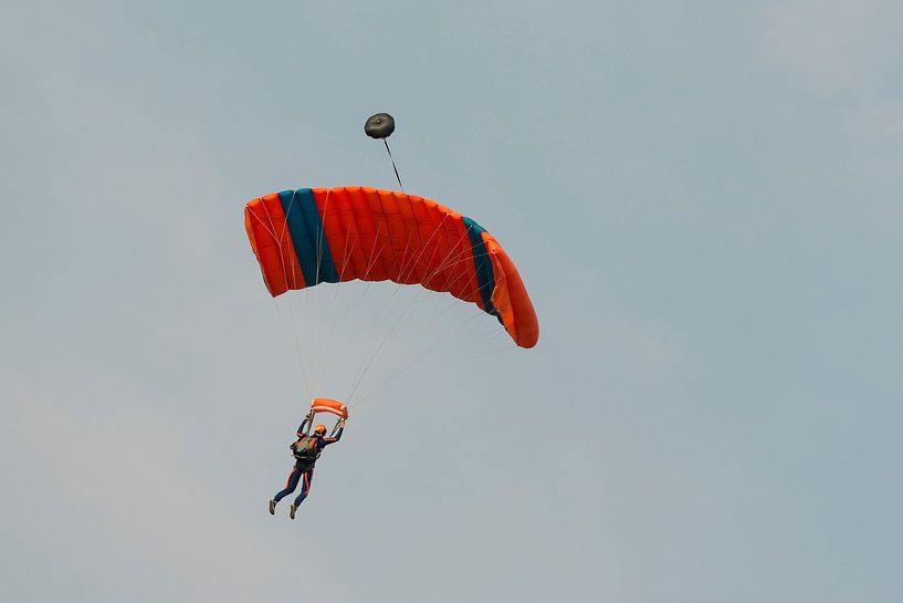 Parachutist tegen een blauwe lucht aan een blauw-oranje parachute von Tonko Oosterink