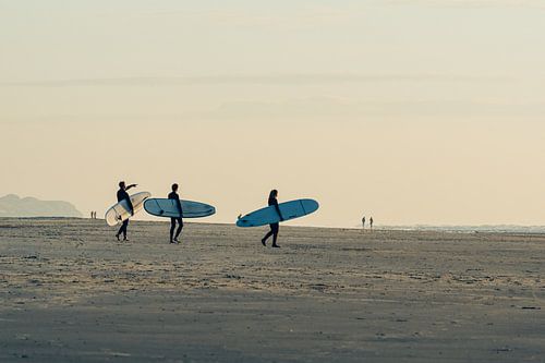 Surfers lopen met hun board richting de zee