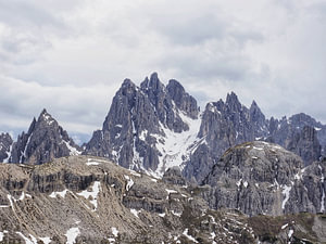 Majestätische Felsformationen ragen eindrucksvoll in den Himmel: Die Drei Zinnen präsentieren sich in perfektem Licht, umgeben von schroffen Gipfeln, alpinen Wegen und karger Hochgebirgslandschaft.