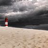Een eenzame vuurtoren staat op een zandduin onder een dreigende, grijze, bewolkte hemel van Thomas Heitz