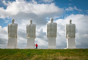 vrouw in rode jas bij de witte Mannenbeelden, Esbjerg, Denemarken. beelden van vier zittende mannen