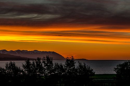 Oranje avondlucht in IJsland uitkijkend over een fjord richting de oceaan