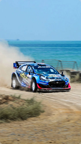 rally car speeding down a dirt road near the seashore