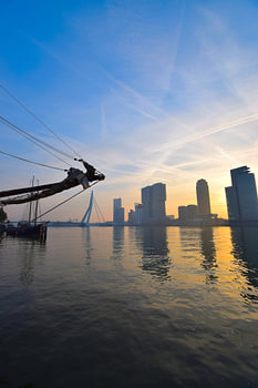 Zonsondergang voor de skyline van Rotterdam met op de voorgrond een zeilschip