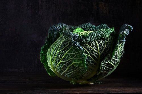green savoy cabbage, a healthy winter vegetable in dramatic light on dark and moody rustic wood with