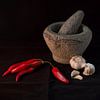 Still life of an Indonesian mortar with red peppers and garlic against a black background (vertical) by Birgitte Bergman