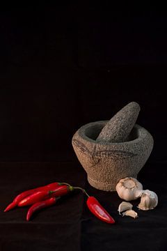 Stilleven van een Tjobek (Indonesische vijzel) met rode pepers en knoflook tegen een zwarte achtergrond (verticaal)