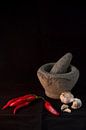 Still life of an Indonesian mortar with red peppers and garlic against a black background (vertical) by Birgitte Bergman thumbnail