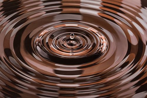 Druppel valt in water waarin bruintinten worden weerspiegeld