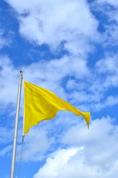Gele wapperende vlag voor een blauwe lucht met wolken van Lilly Wonderz