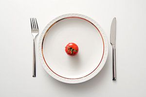 Tomate fraîche dans une assiette avec un bord doré et des couverts sur fond blanc, régime avec des l sur Maren Winter