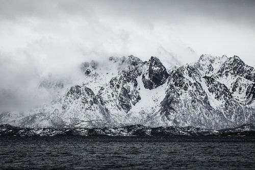 Photo en noir et blanc de nuages bas et de montagnes enneigées. sur Martijn Smeets