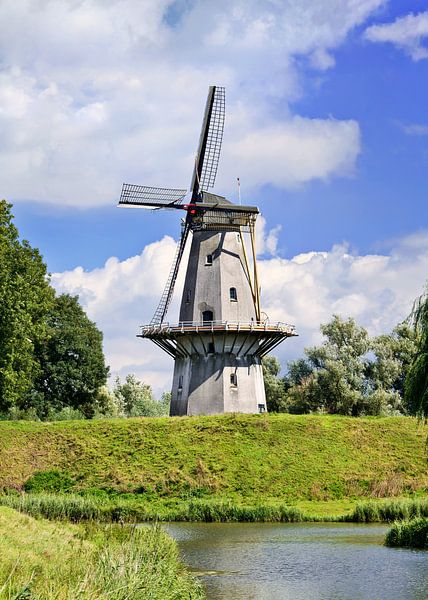 Traditionelle holländische Windmühle auf einem Deich mit blauem Himmel und Wolken von Tony Vingerhoets