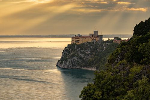 zonneharpen schijnen op Castello di Duino op de rotsen aan de Adriatische kust