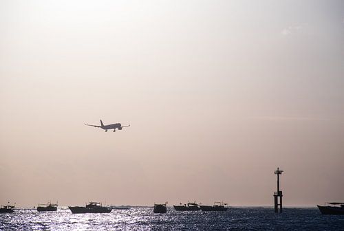 Landend vliegtuig boven zee tijdens zonsondergang