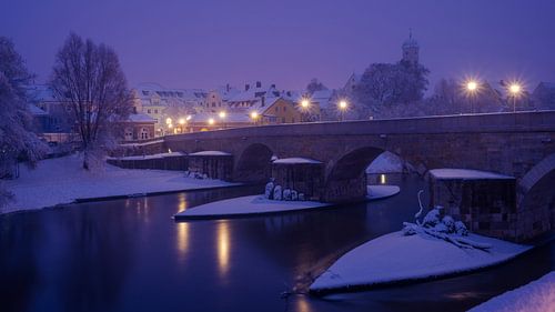 Stone bridge and Stadtamhof in Regensburg at night in winter with snow