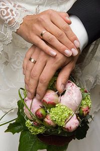 Mains d'un couple de mariés sur le bouquet de la mariée