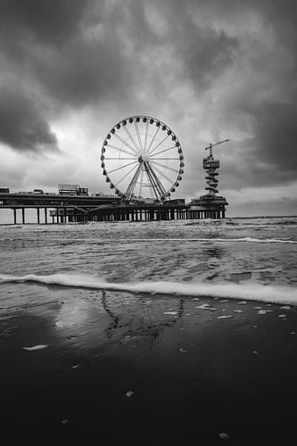 Black and white photo of the beach at scheveningen with a drastic cloud cover over the pier