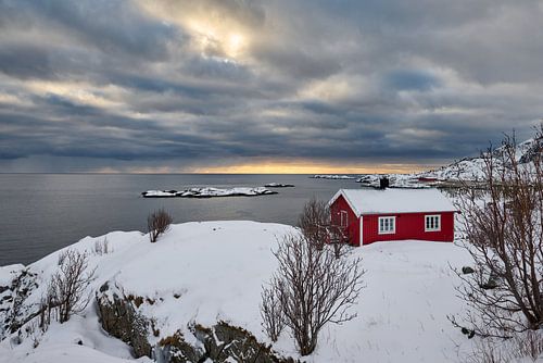 red hut in winter landscape in front of the sea at sunset with clouds