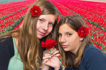 Zwei holländische Mädchen riechen rote Rosen bei Tulpenfeld von Ben Schonewille