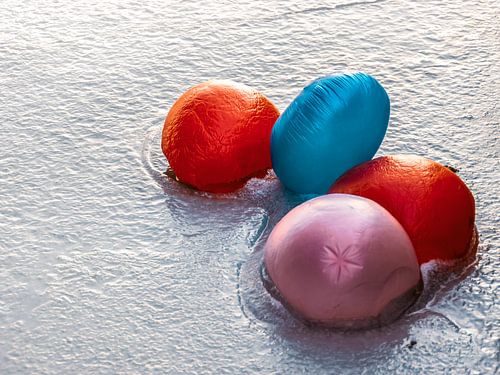 Vier gekleurde kinderballonnen liggen vastgevroren in het ijs