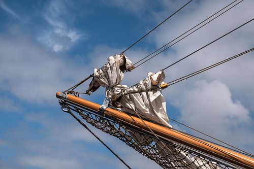 jib boom with reefed sails on the bow of a historic sailing ship against a blue sky with clouds, cop