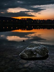 Sonnenuntergang am See mit einem Stein im Vordergrund