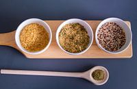 Houten plank met quinoa, rijst en couscous in witte schaaltjes - houten lepel met kruiden